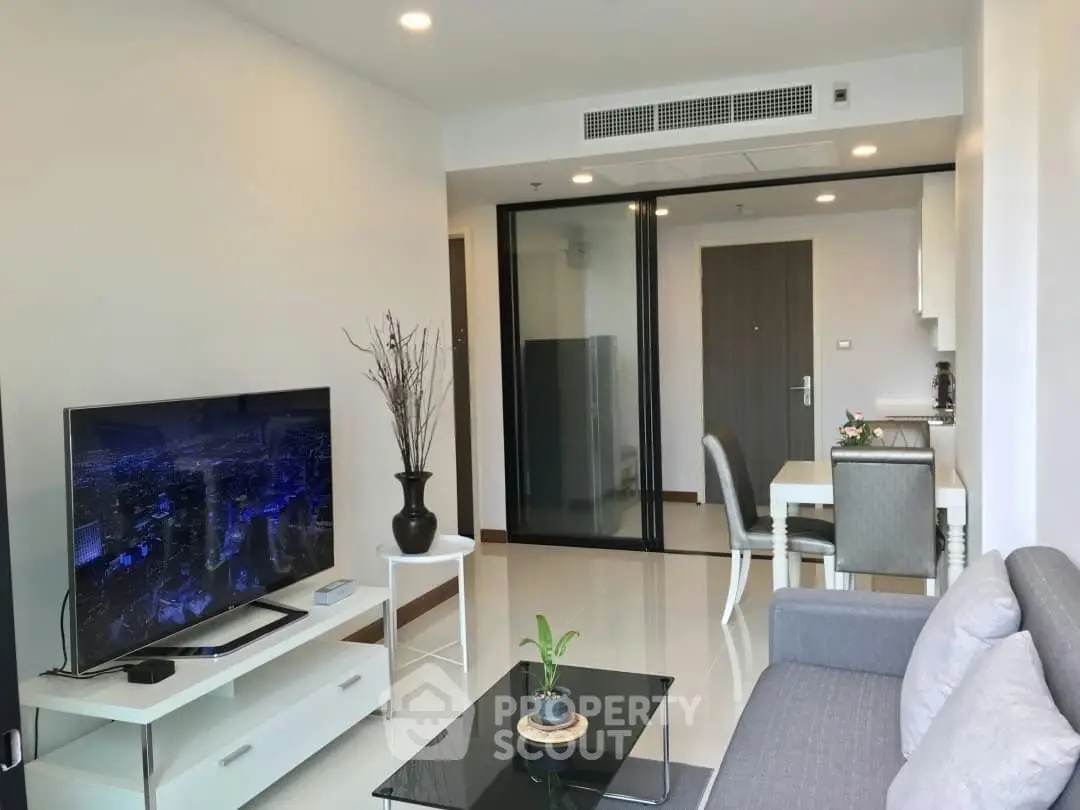 Modern living room with sleek furniture and open layout, featuring a large TV and elegant decor.