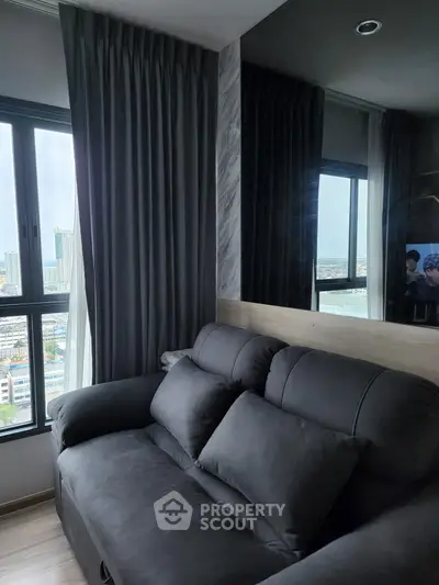 Modern living room with city view, featuring sleek black sofa and large windows.