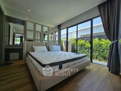 Spacious bedroom with large windows and garden view, featuring modern decor and wooden flooring.