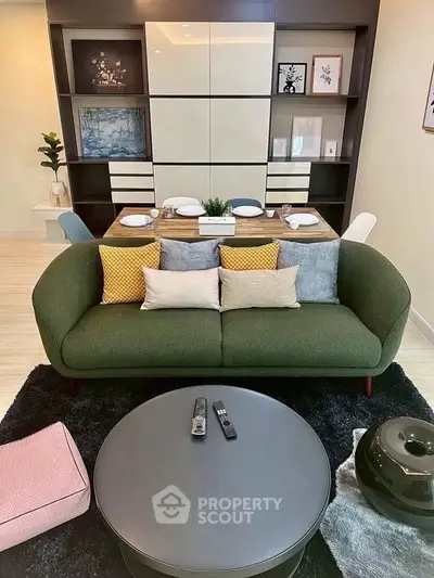 Stylish living room with modern decor, featuring a cozy green sofa, elegant dining setup, and chic shelving.