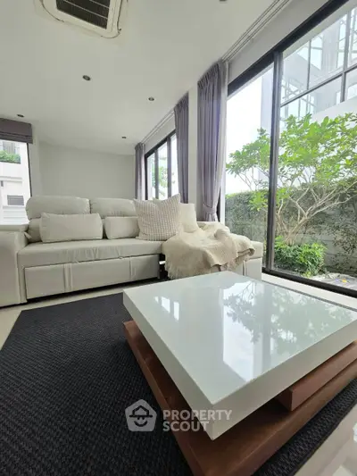 Modern living room with large windows and stylish furniture, offering a serene garden view.