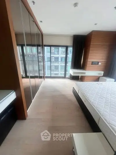 Spacious modern bedroom with large windows and sleek wooden accents in a high-rise apartment.