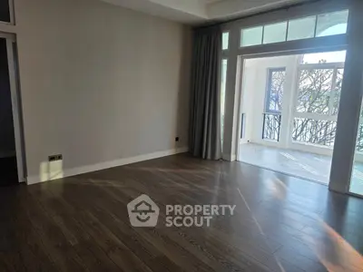 Spacious living room with elegant wooden flooring and large windows leading to a balcony.
