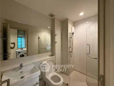 Modern bathroom with glass shower and washing machine in sleek apartment.