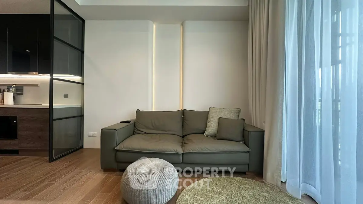 Modern living room with sleek sofa, cozy cushions, and elegant lighting, adjacent to a stylish kitchen area.