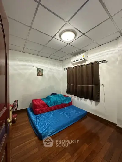 Cozy bedroom with wooden flooring and air conditioning, featuring a simple bed setup and natural lighting.