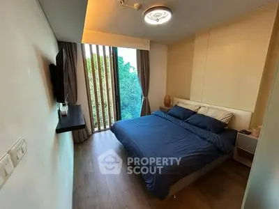 Cozy bedroom with large window and modern decor, offering serene views of lush greenery.