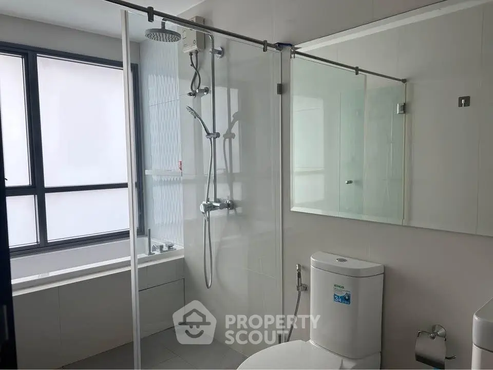 Modern bathroom with glass shower and bathtub in sleek apartment.