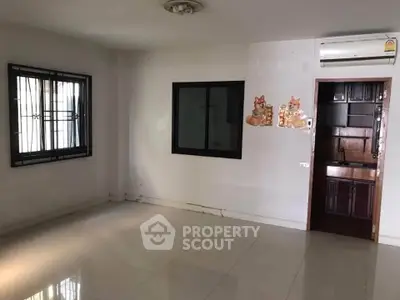 Spacious living room with tiled flooring and air conditioning, featuring a small kitchenette area.