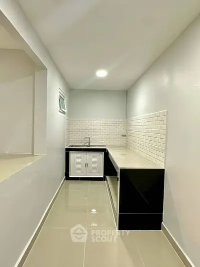 Modern minimalist kitchen with sleek black and white design and glossy tiled floor.