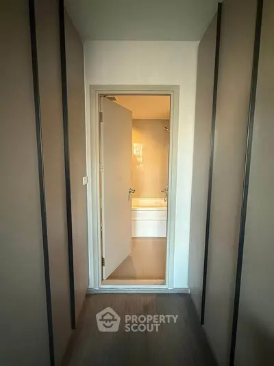 Modern hallway leading to a sleek bathroom with a bathtub, showcasing minimalist design and warm lighting.
