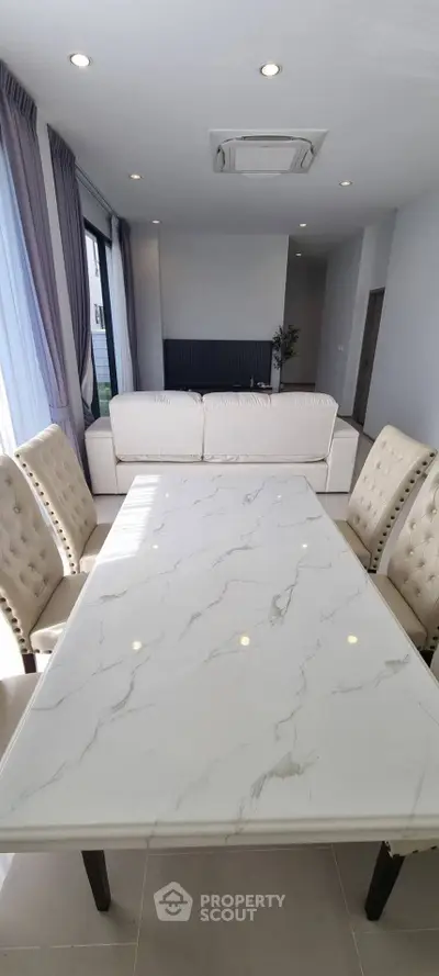 Elegant dining area with marble table and plush chairs in a modern open-plan living space.