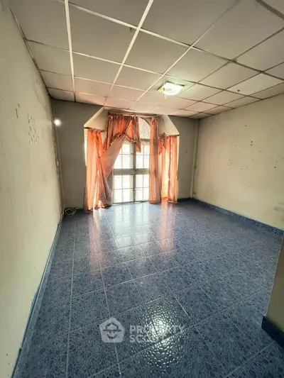 Spacious room with blue tiled floor and large window, ideal for customization.