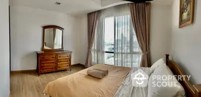 Spacious bedroom with large windows offering ample natural light and a serene view, complemented by elegant drapery and classic wooden furniture.