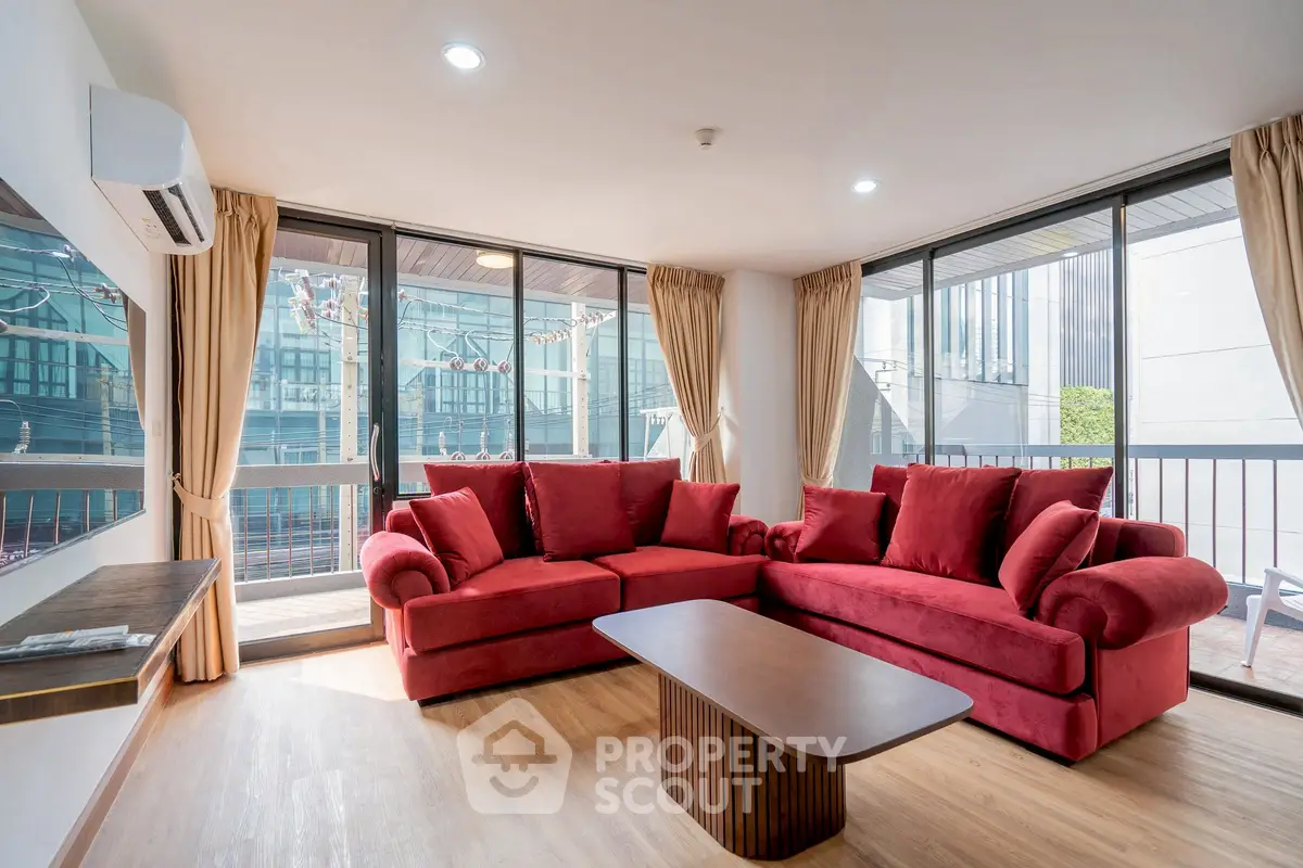 Spacious living room with red sofa and large windows offering city view