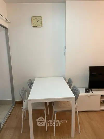 Modern dining area with sleek white table and chairs, adjacent to a cozy living space with TV setup.
