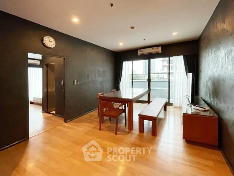 Spacious living room with wooden flooring and modern furniture, featuring a large window with balcony access.