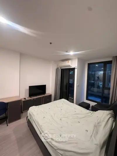 Modern bedroom with cozy bed, TV, and large window offering natural light in a stylish apartment.