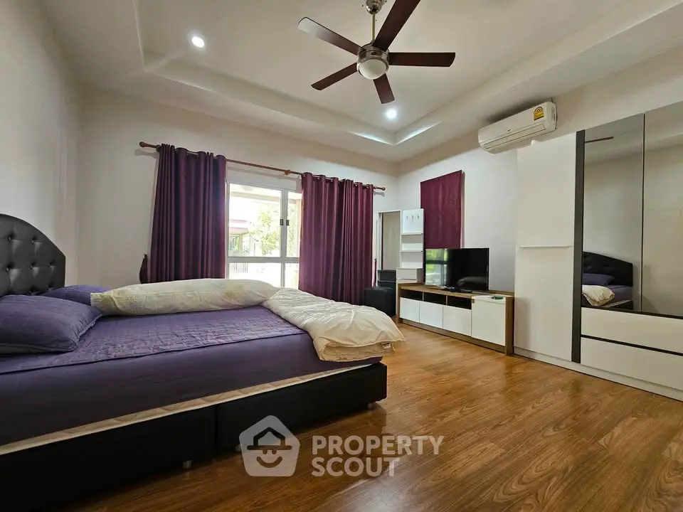 Spacious bedroom with modern furnishings and natural light, featuring a ceiling fan and air conditioning.