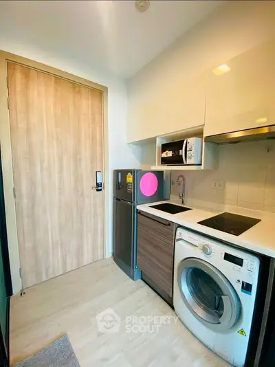 Modern compact kitchen with washing machine and sleek cabinetry in a cozy apartment.