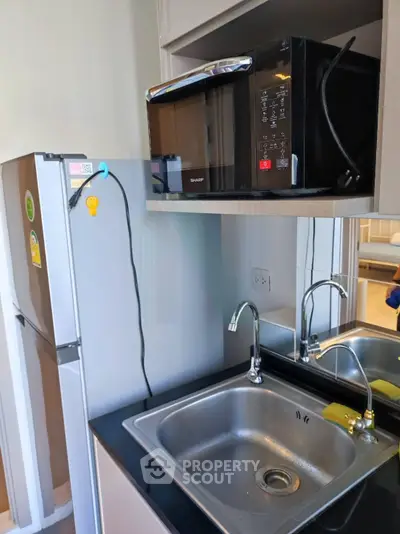 Modern kitchen with stainless steel sink, microwave, and fridge in compact layout.