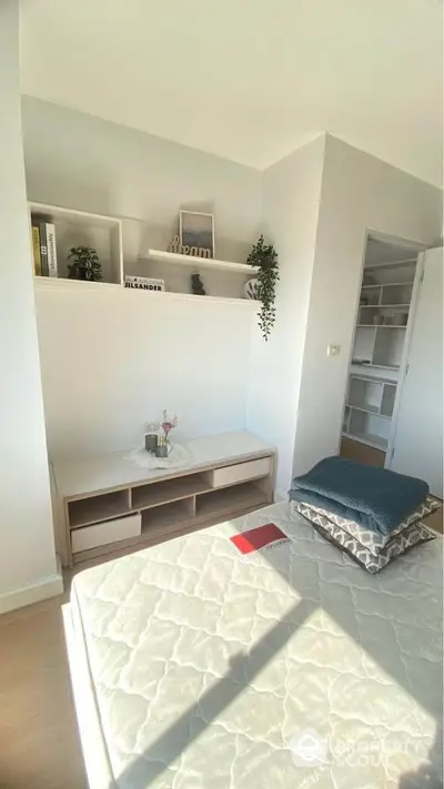 Bright and airy bedroom with a cozy mattress on the floor, built-in shelving, and a minimalist TV stand, perfect for modern living.