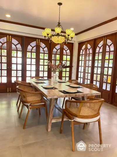 Elegant dining room with wooden table and chairs, surrounded by large windows and stylish lighting.