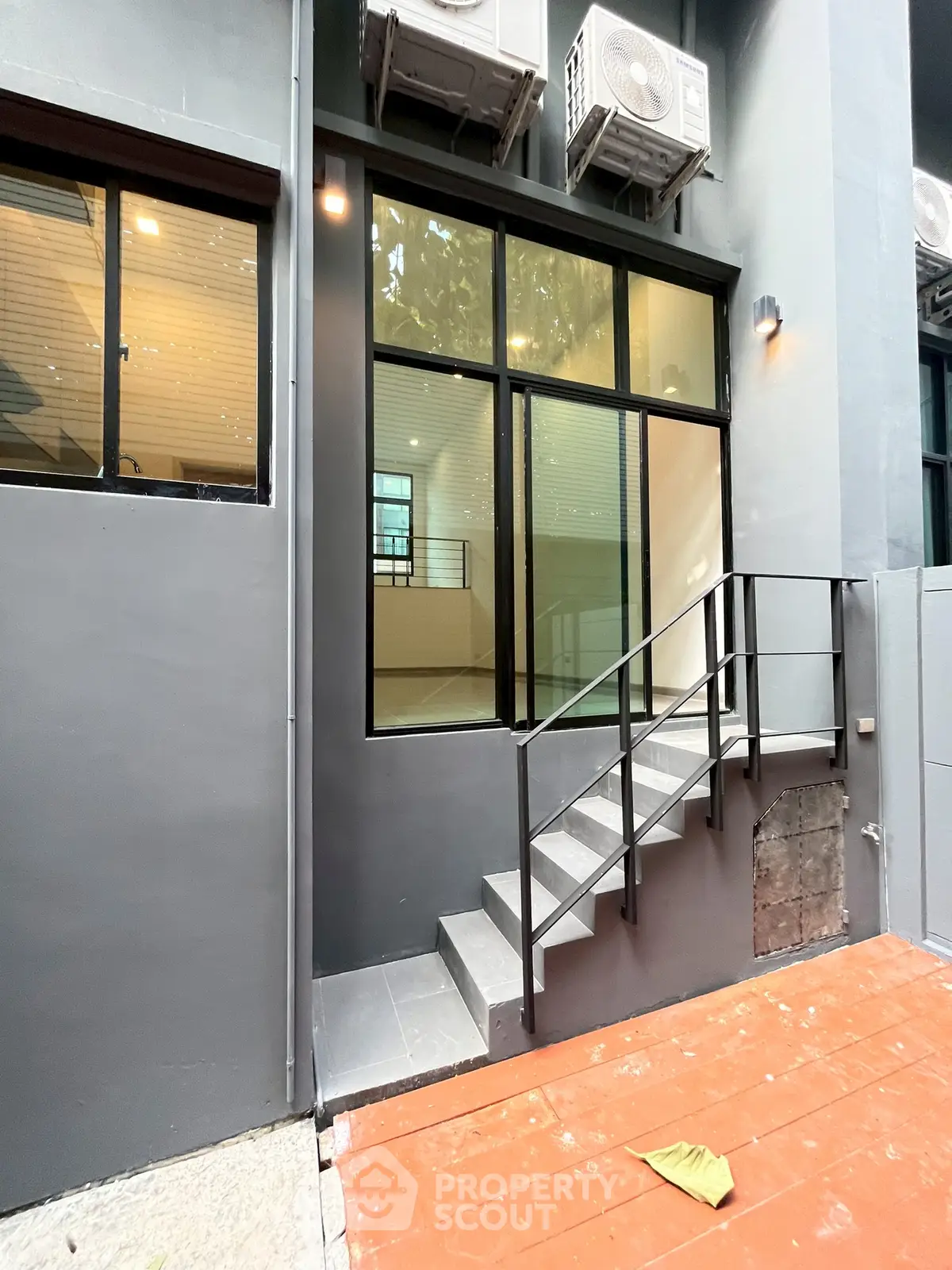 Modern building exterior with sleek windows and air conditioning units, featuring a small staircase and contemporary design.