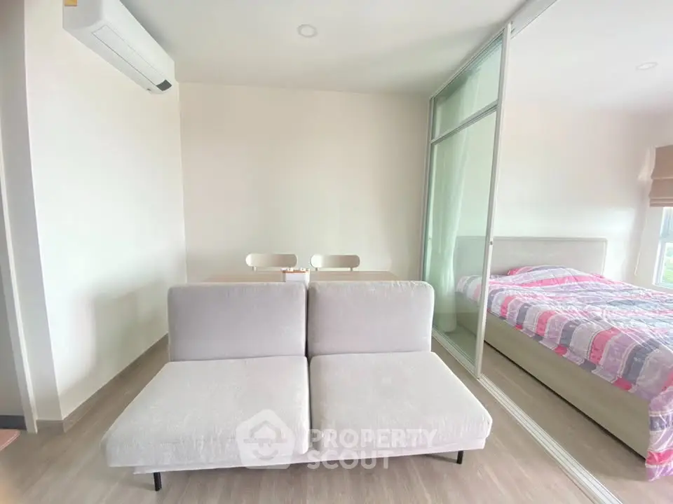 Modern living room with cozy sofa and adjacent bedroom in open-plan apartment.