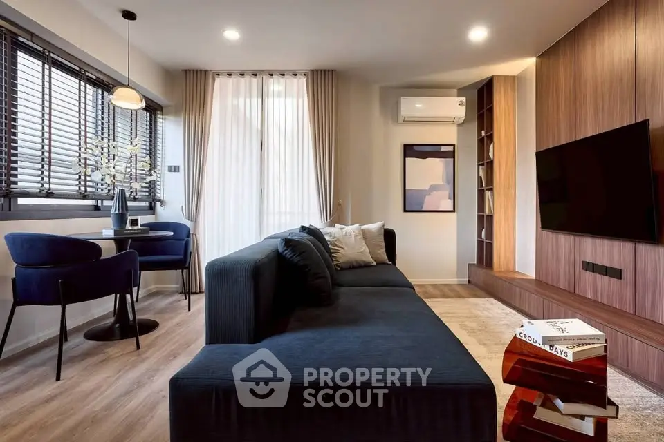 Modern living room with stylish decor, large sofa, and dining area, featuring elegant lighting and wooden accents.
