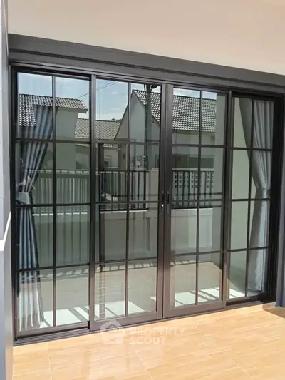 Modern sliding glass doors leading to a spacious balcony with a view of neighboring houses.