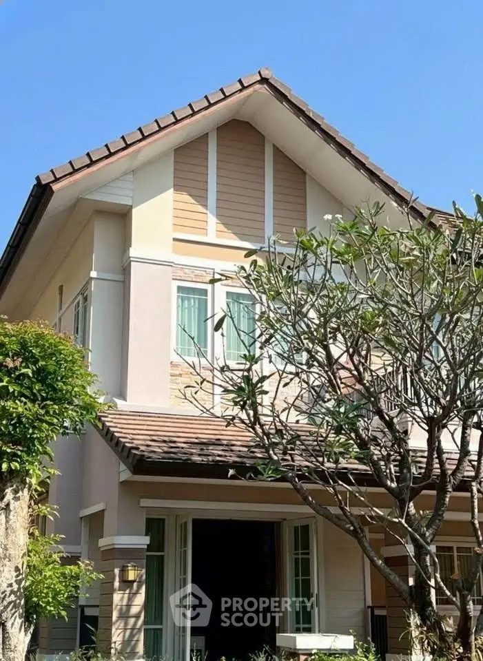 Charming two-story house with lush garden and classic architecture under clear blue sky.