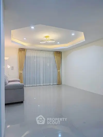 Spacious modern living room with elegant ceiling design and large window draped with curtains.