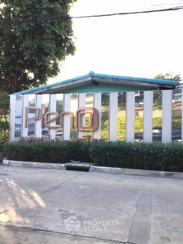 Modern real estate entrance with stylish signage and lush greenery, showcasing contemporary architectural design.