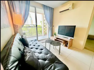 Modern living room with balcony view, sleek black sofa, and flat-screen TV.