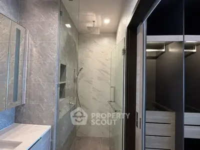 Luxurious modern bathroom with sleek shower and adjacent walk-in closet, featuring elegant tile design.