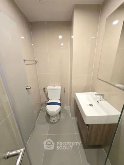 Modern bathroom with sleek fixtures and neutral tiles, featuring a compact design for efficient space use.