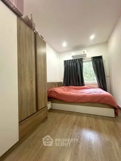 Cozy bedroom with wooden flooring and modern furnishings, featuring a comfortable bed and ample natural light.