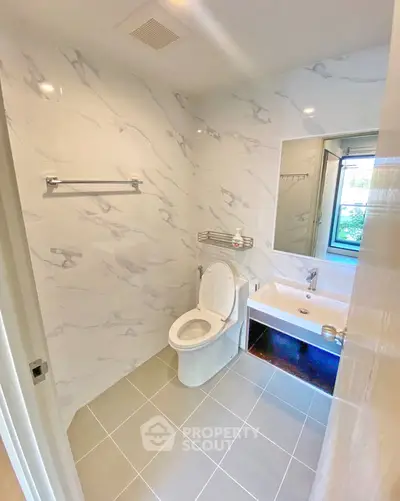 Modern bathroom with marble walls and sleek fixtures, featuring a toilet and a stylish sink under a large mirror.