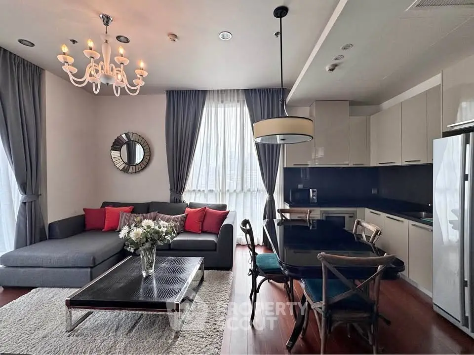 Elegant living room with modern kitchen, stylish chandelier, and cozy seating area.