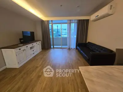 Spacious living room with modern furniture and balcony view, featuring wooden flooring and air conditioning.