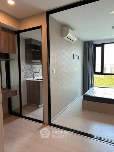 Modern apartment interior with bedroom and kitchenette, featuring sleek design and large windows for natural light.