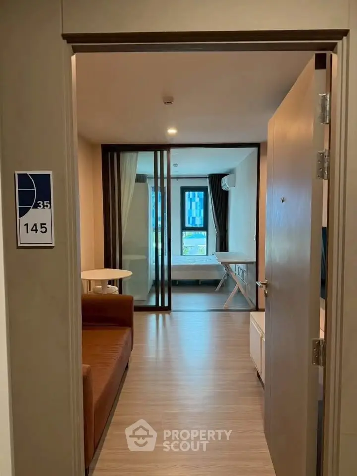 Modern apartment entrance with open door leading to stylish living area and large windows.