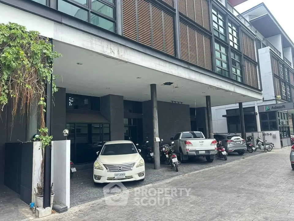 Modern building exterior with parking area and vehicles, showcasing urban architecture.