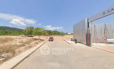 Vacant land with clear skies, potential for development, surrounded by greenery and construction fencing.
