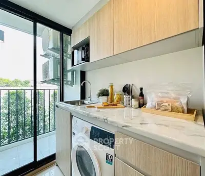 Modern kitchen with washing machine and balcony view, sleek cabinetry and marble countertop.