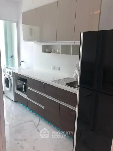 Modern kitchen with sleek cabinets, washing machine, and fridge in a compact layout.
