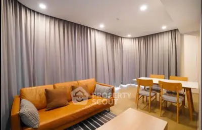 Modern living room with stylish leather sofa and dining area, featuring elegant lighting and floor-to-ceiling curtains.