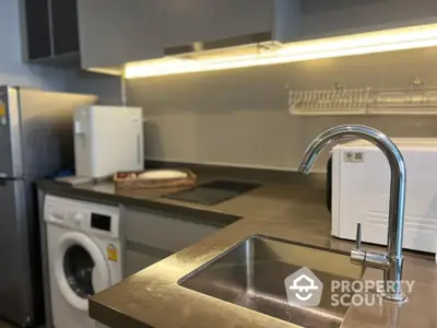 Modern kitchen with stainless steel sink, under-cabinet lighting, and integrated appliances including a washing machine and fridge, showcasing a blend of functionality and sleek design.