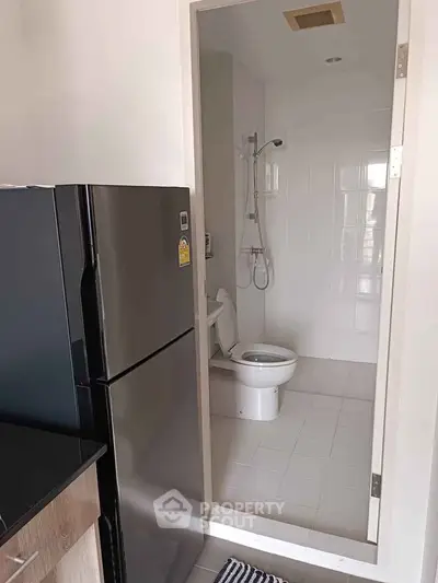 Compact bathroom with modern shower and adjacent black refrigerator